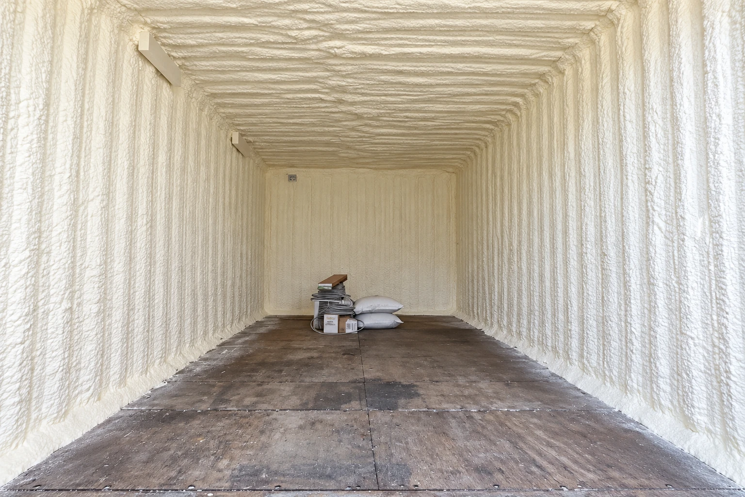 Narrow room with thick closed-cell spray foam covering the walls and ceiling above a bare concrete floor.