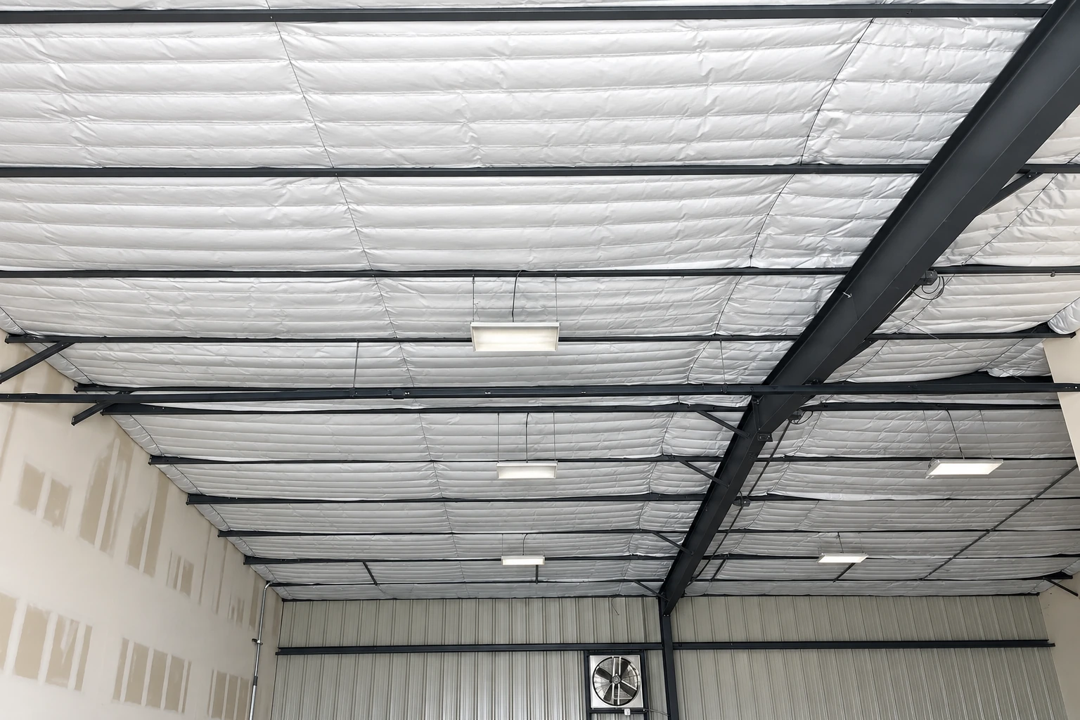 White insulated panels cover the ceiling of a large commercial building, supported by dark steel beams and lit by hanging fixtures.