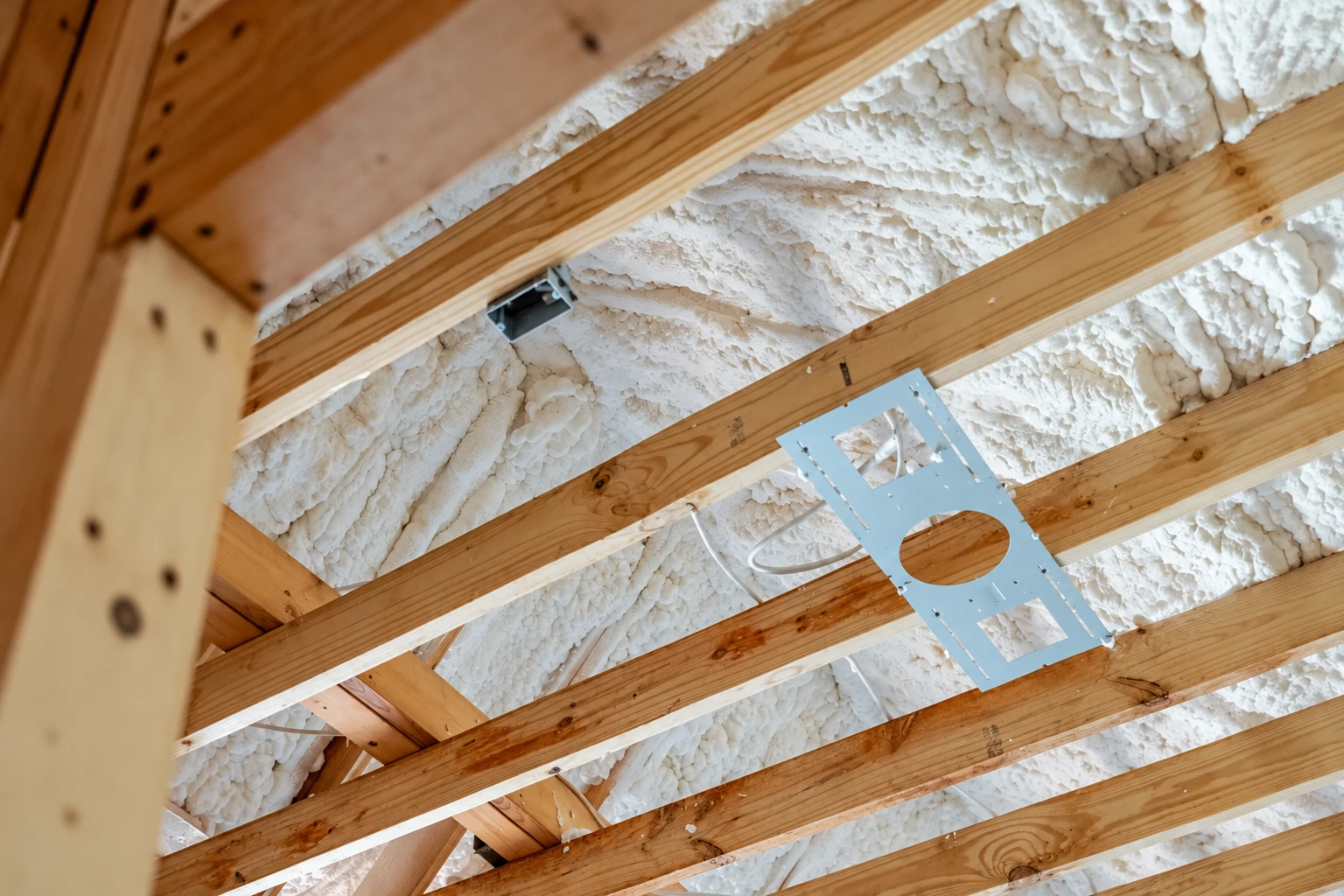 White open-cell spray foam coats the underside of a roof between exposed wooden rafters.